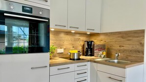 A modern kitchen with white cabinets, a built-in oven, a coffee maker, and a sink. - 005 - Hooge (BC.n3) - BUE - Apartment house Seewind (Büsum)