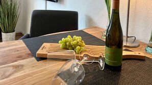 A hotel room with a television, a framed picture of fruits, a table with a bottle of wine, glasses, and a red tulip. - 005 - Hooge (BC.n3) - BUE - Apartment house Seewind (Büsum)