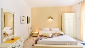 Une chambre à coucher comprenant un lit, une table de chevet, un miroir, une armoire et un luminaire fixé au mur.
