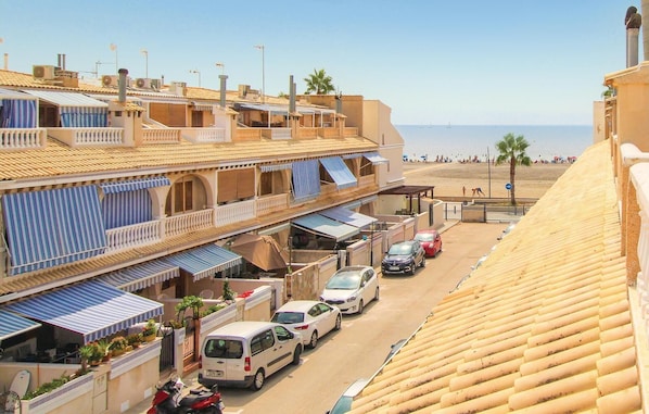 Eine Küstenstraße mit Gebäuden, geparkten Autos und einem Strand im Hintergrund.