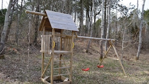 A wooden playhouse with a sloped roof and a swing set in a wooded area. - Lovely home in Sæby with WiFi (Sæby)
