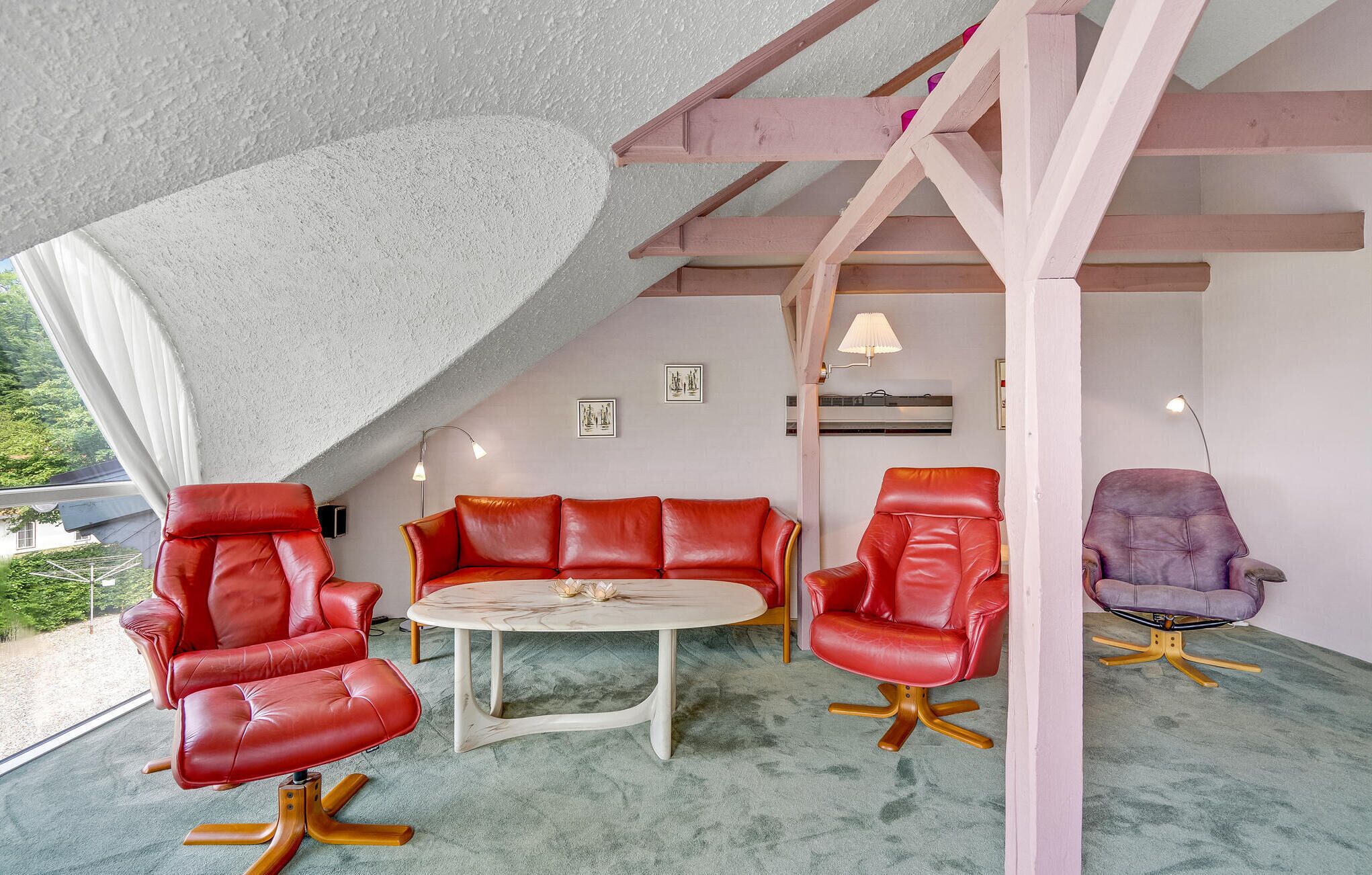 Una habitació acollidora amb un sostre inclinat, un sofà de pell vermella, una taula de centre rodona i un butac armchair morat.