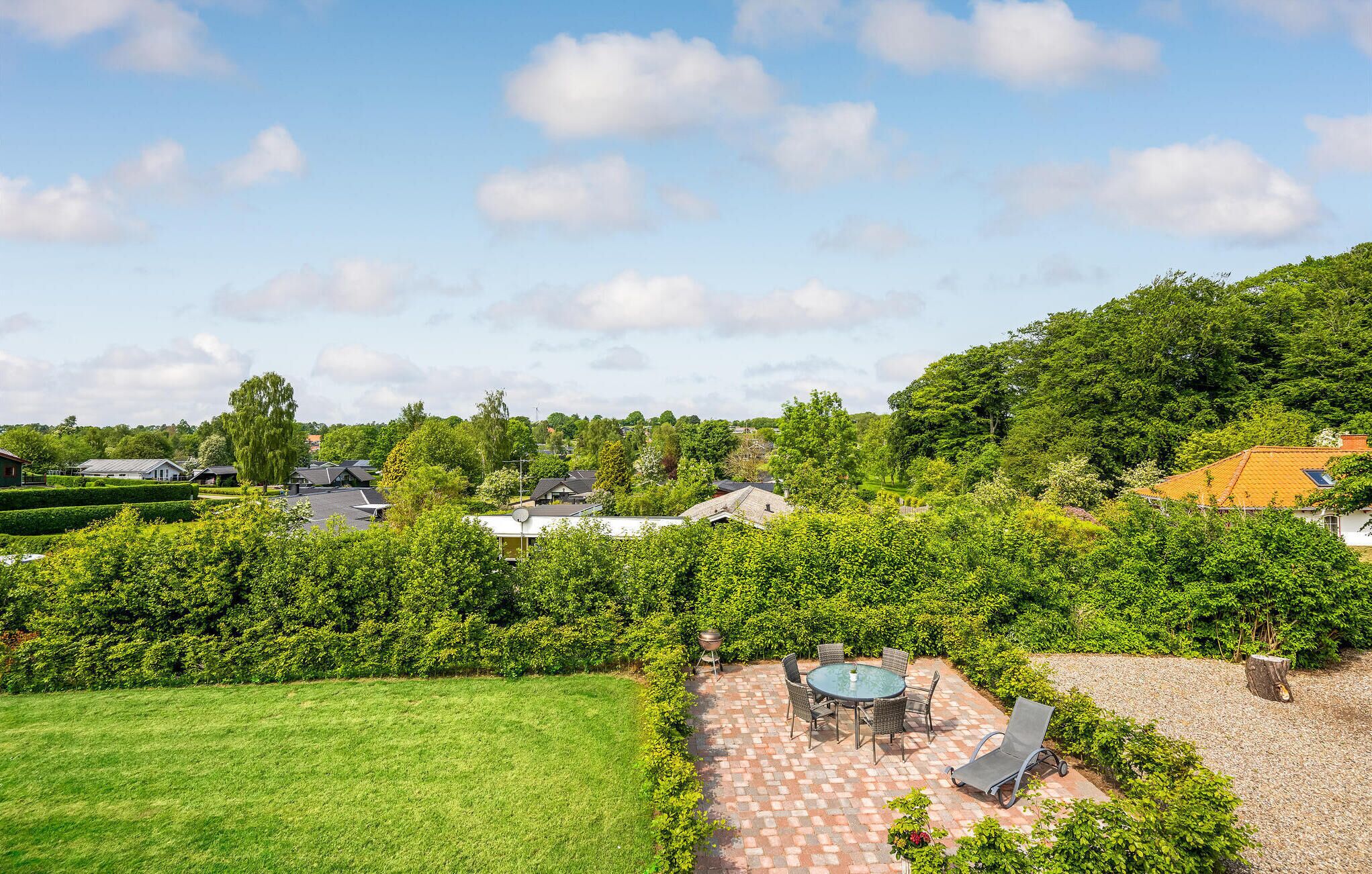 Un quartier résidentiel doté d’une pelouse bien entretenue, d’une terrasse avec mobilier d’extérieur et d’une vue sur les maisons et les arbres des environs.