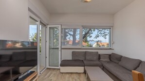 En moderne stue med en modulsofa, et fladskærms-tv og en skydedør, der fører ud til en balkon.