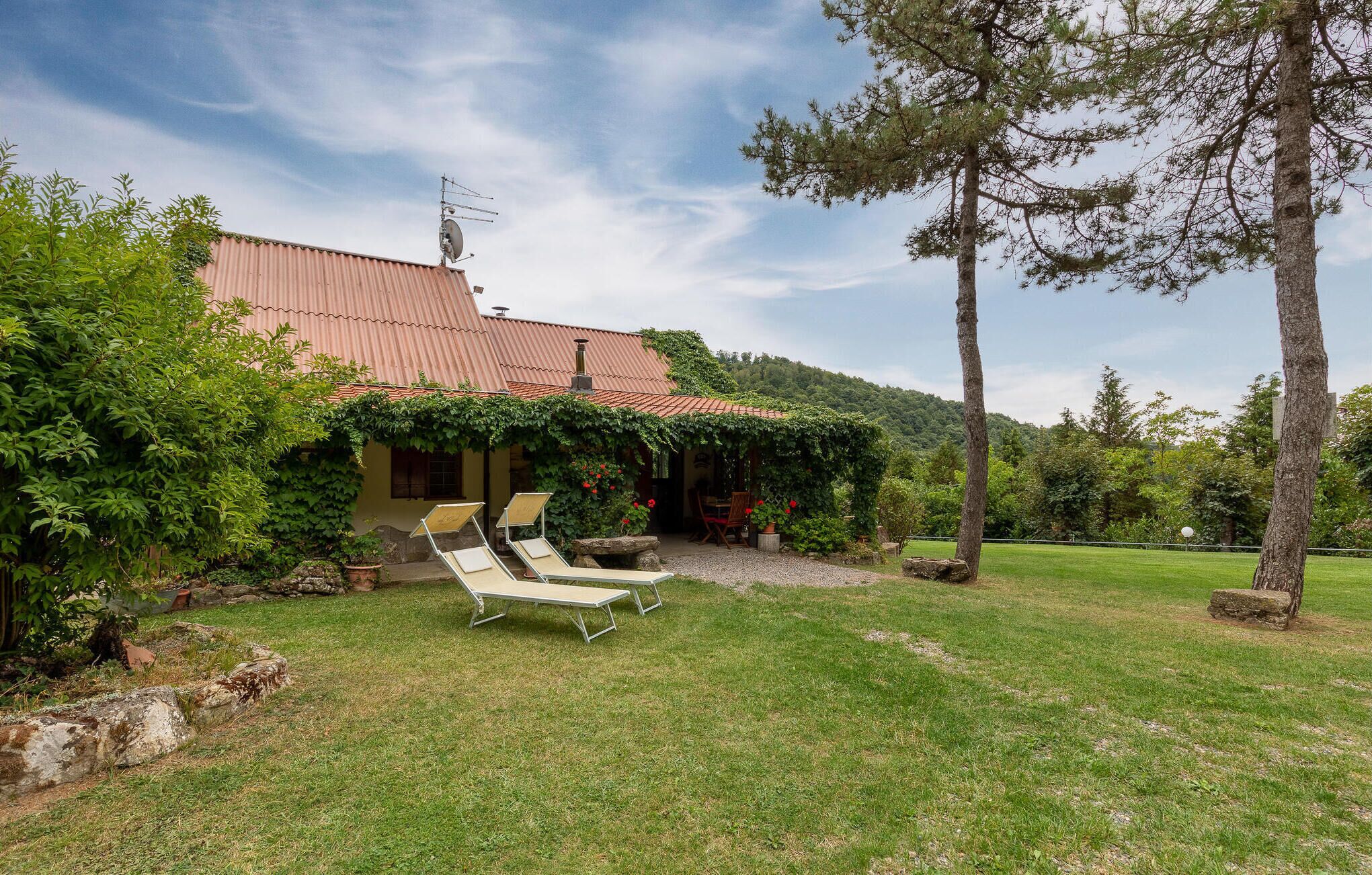 Une maison avec un toit rouge, un jardin avec une pelouse et deux fauteuils de jardin.