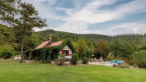Ein rustikales Haus mit rotem Dach, umgeben von üppiger grüner Landschaft und einer Bergkulisse.