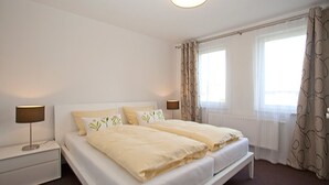 Een tweepersoonsbed met witte lakens en een nachtkastje met een lamp.