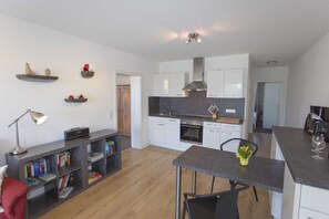 A modern kitchen with white cabinets, a central island, and a dining area with a table and chairs. - Apartment 1 - Rügen-Fewo 280/1 (Dreschvitz)