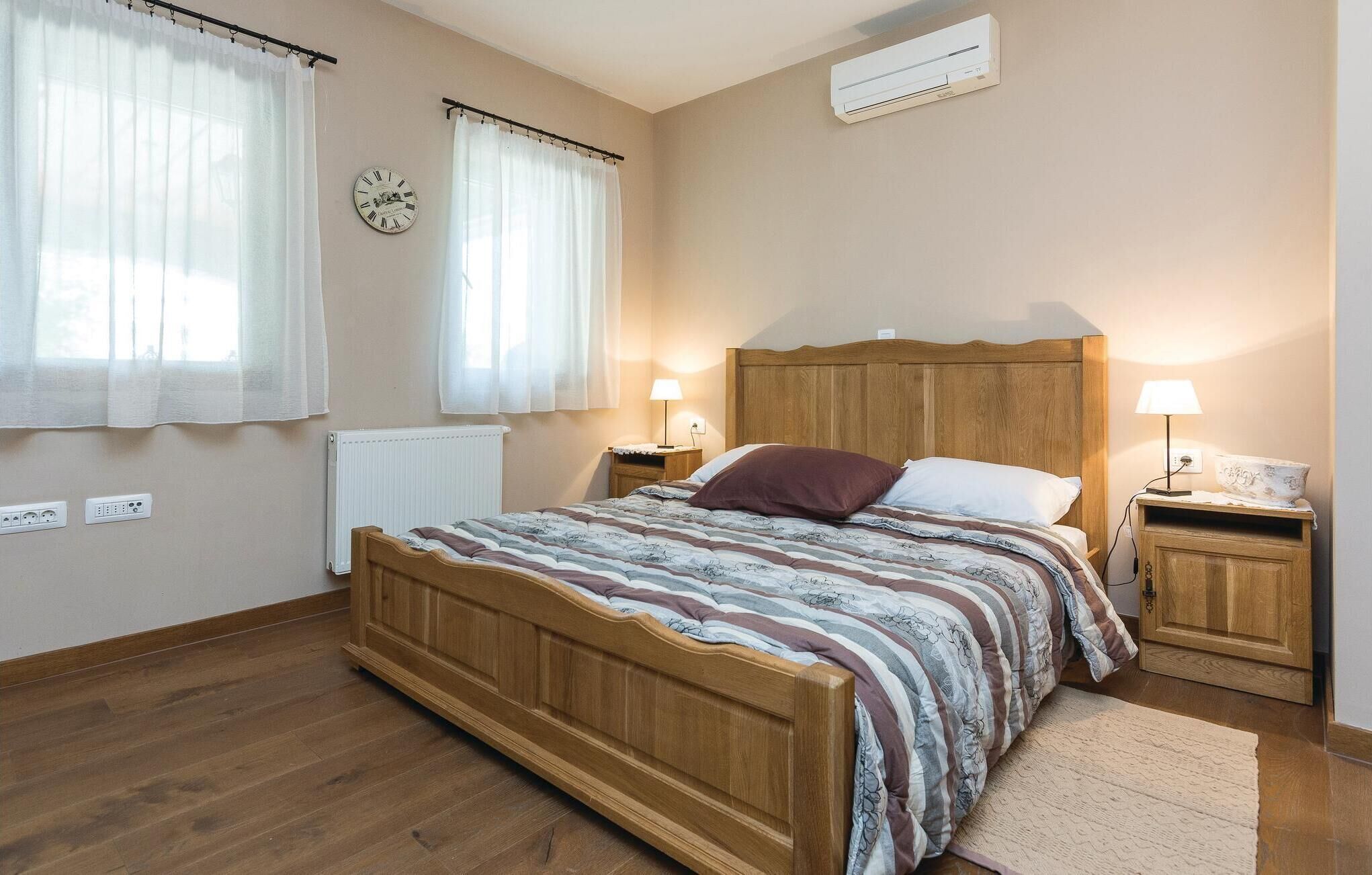 A bedroom with a wooden bed, two bedside tables with lamps, a radiator, and a clock on the wall.