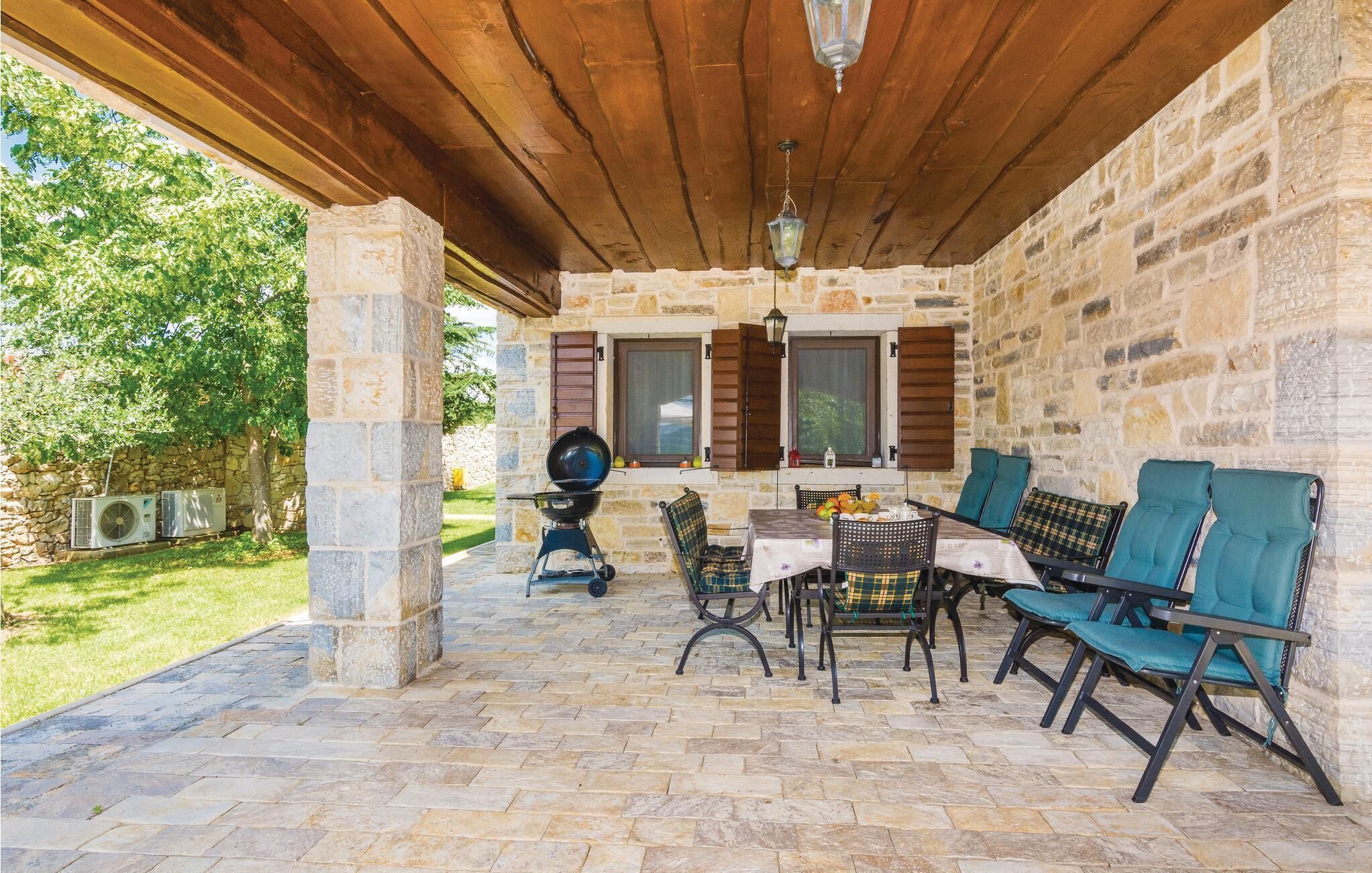 An outdoor patio with stone walls, wooden beams, and a grill.