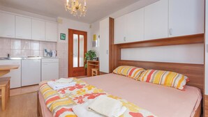 Una habitación de hotel con cama, cabecera de madera, escritorio, kitchenette y candelabro.