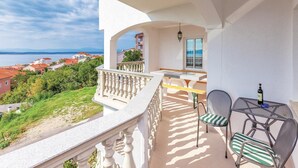 Un balcón con vistas al mar y edificios, una mesa con sillas y una botella sobre la mesa.