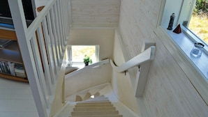 Un escalier avec une rampe, une petite fenêtre en haut et une vue sur la verdure à l’extérieur.