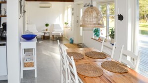 Une cuisine moderne avec des meubles blancs, une table à manger en bois agrémentée de sets de table en fibres naturelles, et une grande fenêtre donnant sur un paysage verdoyant.