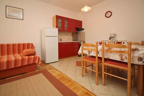 A compact living space with a kitchenette, a dining area with wooden chairs, a striped sofa, and a small rug. - Holiday apartment on the water with balcony (Šilo)