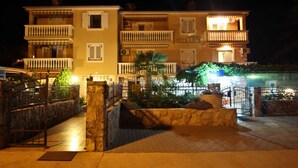 Un immeuble à plusieurs étages doté de balcons, d’une entrée sécurisée et d’une zone pavée agrémentée de plantes.