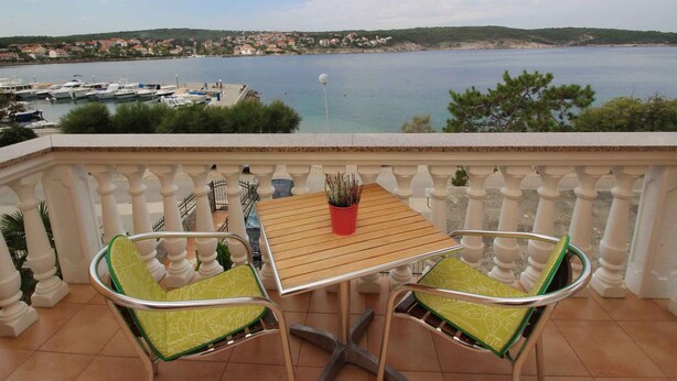 Un balcon avec une table et deux chaises, donnant sur une marina et une ville côtière.