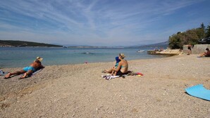 Une plage où l’on peut voir des gens se prélasser au soleil et nager, un ciel dégagé et une vue lointaine sur la terre ferme.