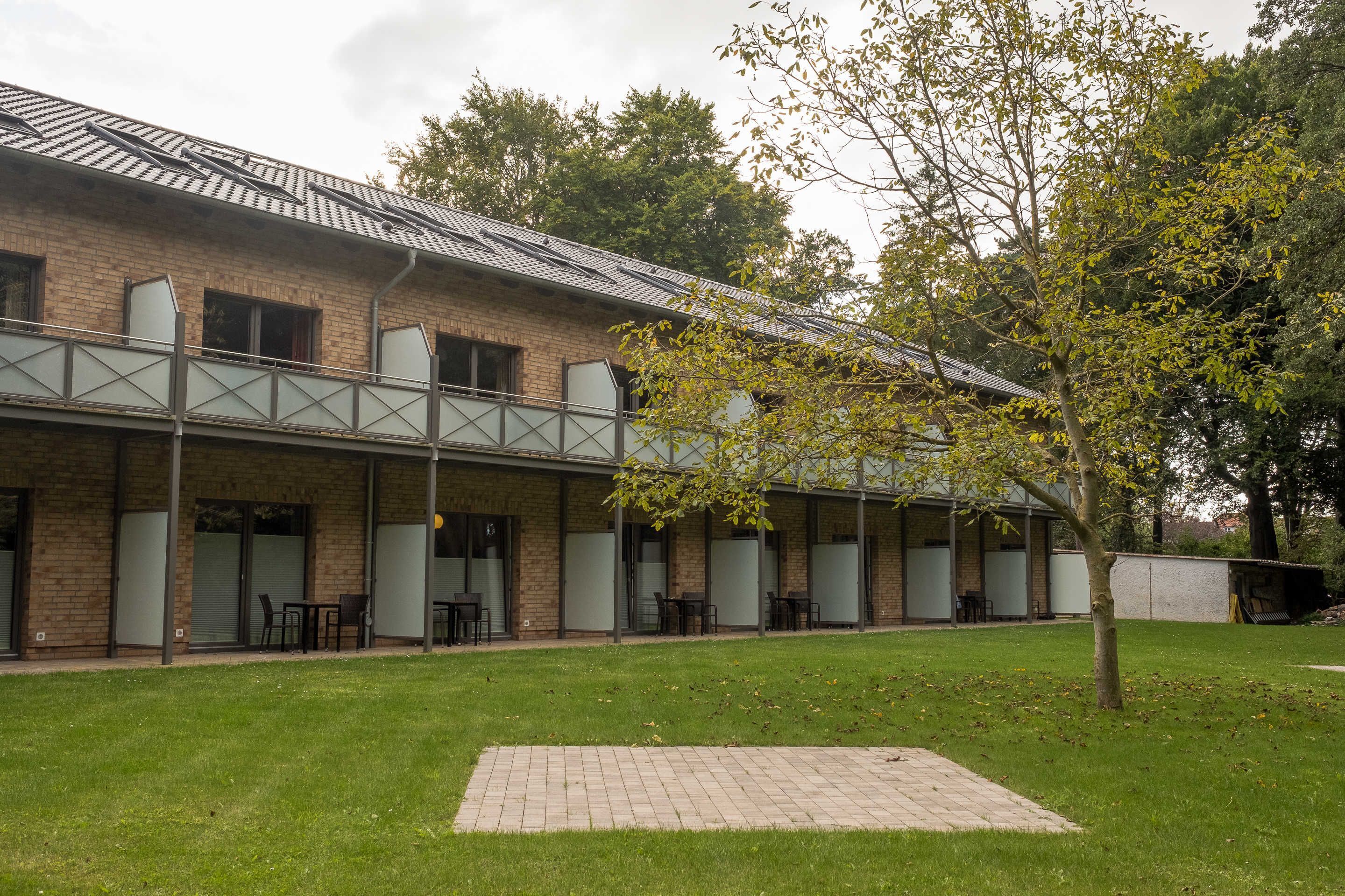 Un bâtiment à la façade en briques, doté de grandes fenêtres et d’un espace extérieur abrité avec des tables et des chaises.