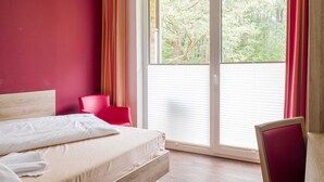 Un dormitorio con una cama, un sillón rojo y vistas a árboles a través de una ventana.