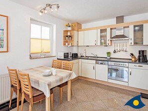 Une cuisine moderne avec des meubles blancs, une table à manger avec des chaises, un four à micro-ondes, une cuisinière et un évier.