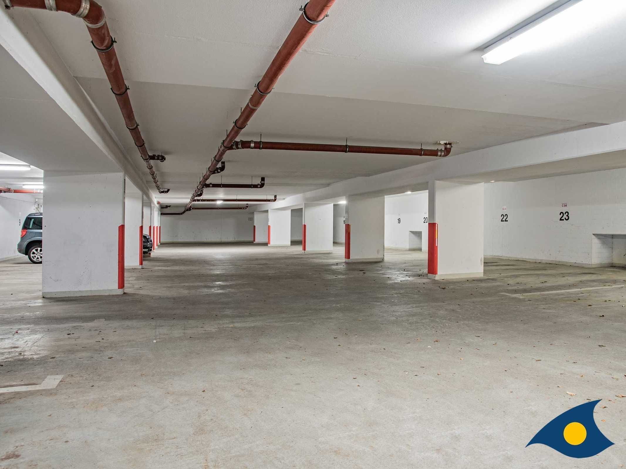 An empty parking garage with white walls, numbered parking spaces, and visible red pillars.