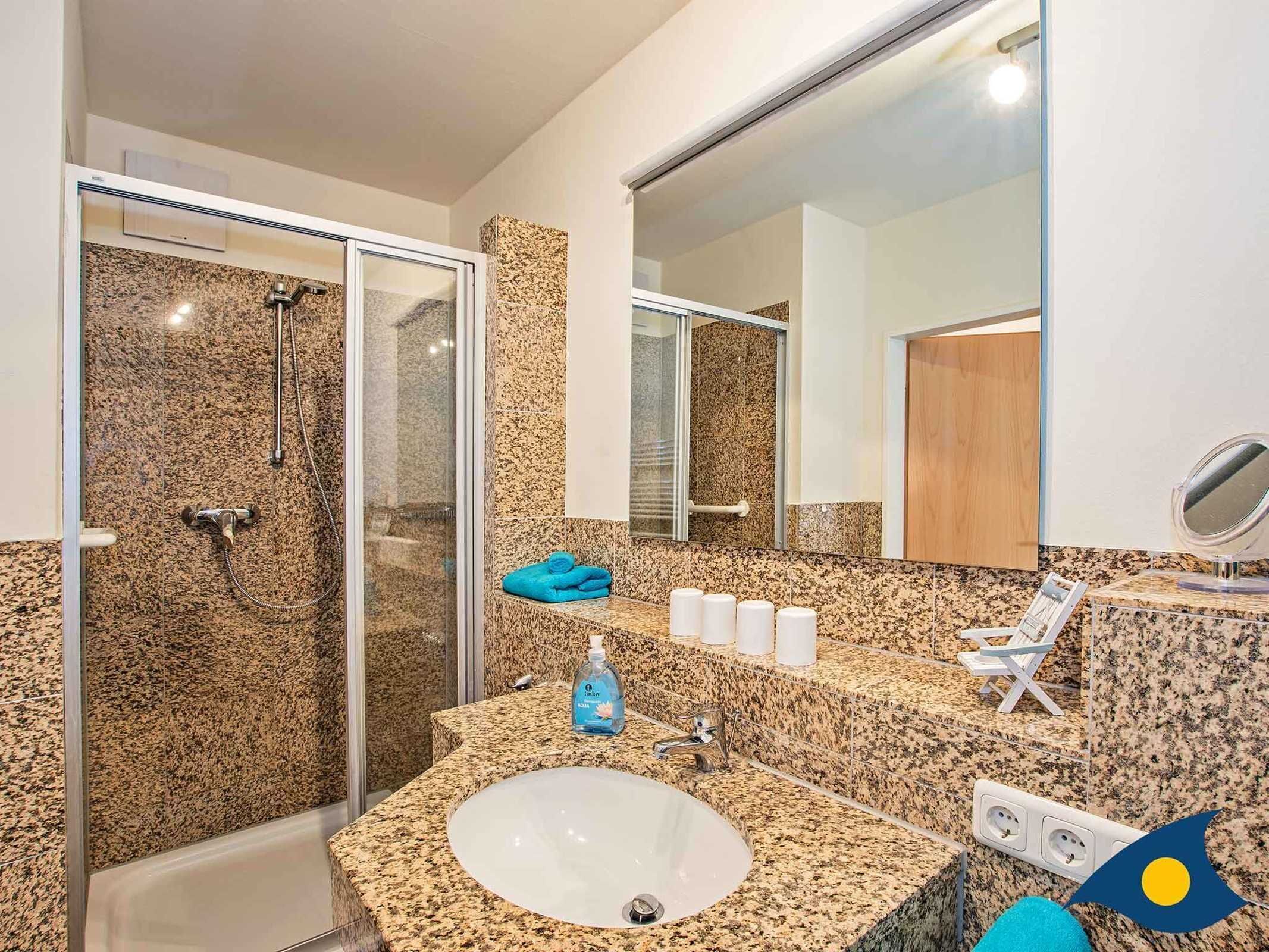 A bathroom with a granite countertop, a sink, a glass shower enclosure, a mirror, and a towel rack.