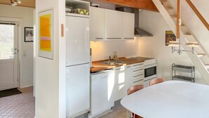 A modern kitchen with white cabinets, a wooden countertop, and a built-in oven. There is a dining area with a white table and chairs. - 1 bedroom lovely home in Kalundborg (Kalundborg)