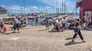 Un puerto deportivo con barcos amarrados, gente caminando y un edificio con un cartel.