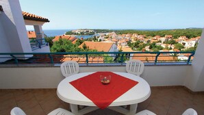 En balkon med et bord og stole, der udover et kystby med bygninger med terracotta-tag.