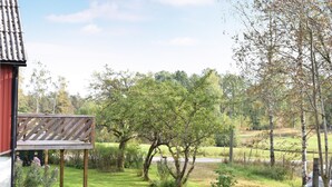 A red building with a wooden deck, surrounded by a grassy area with trees and a fence. - 2 bedroom beautiful home in örkelljunga (Örkelljunga)