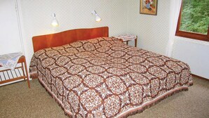 Quarto com colcha estampada, duas luminárias de cabeceira, uma mesinha com um vaso e uma janela com vista para o verde.