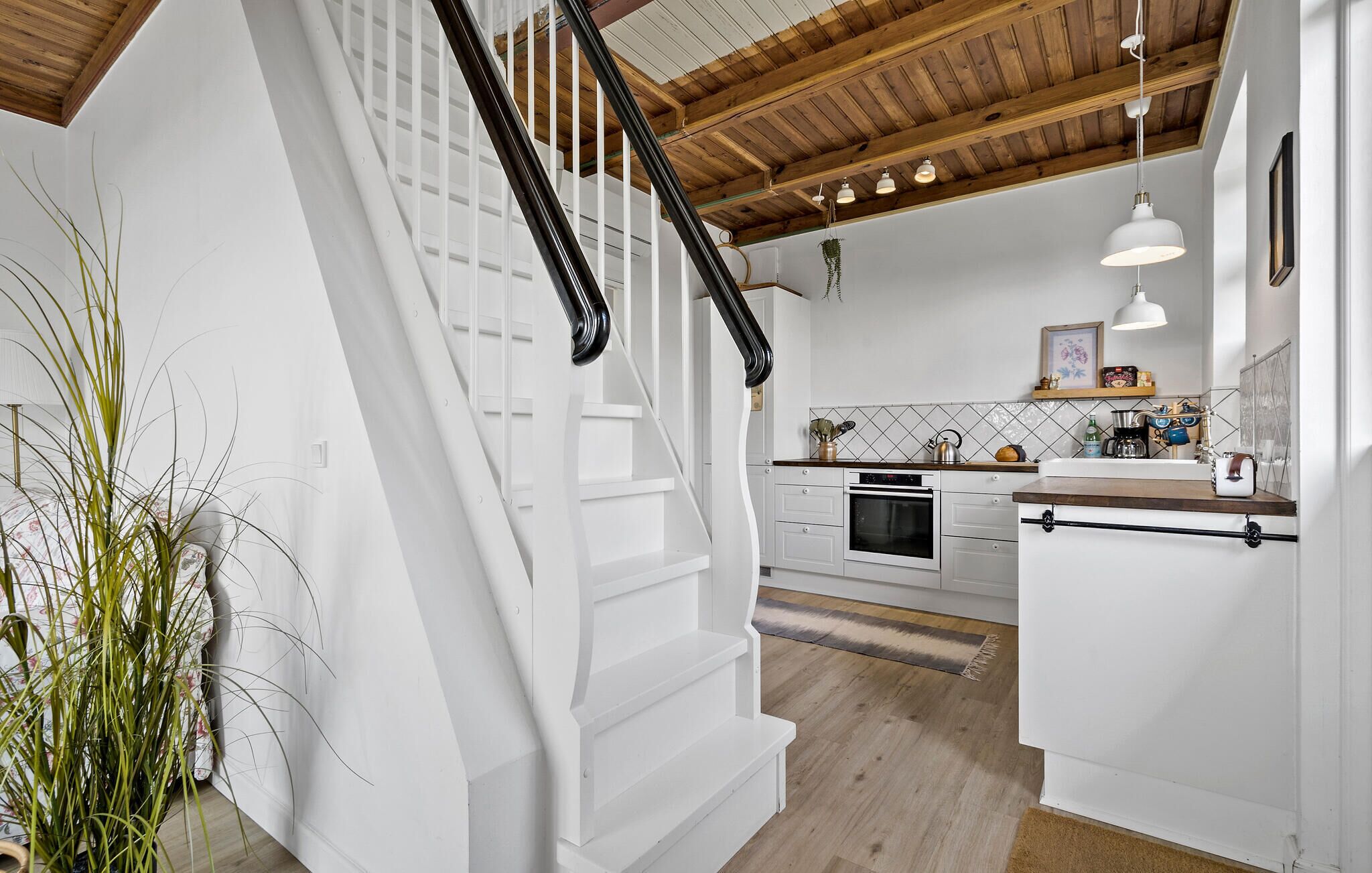 Una cocina moderna con armarios blancos, una escalera de madera y una lámpara colgante.