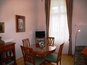 A dining area with a round table, chairs, a small TV on a stand, and a bookshelf.
