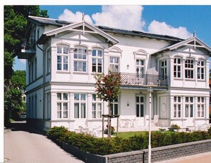 A large, white, two-story building with a symmetrical facade, multiple windows, and a balcony.