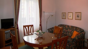 Una sala de estar con una mesa redonda de comedor, dos sillas, un sofá, un televisor y tres cuadros en la pared.