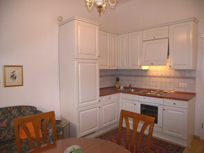 A compact kitchen with white cabinets, a wooden dining table, and a floral-patterned sofa.