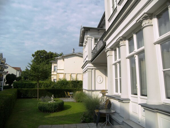 A building with a white facade, large windows, and a small garden area with a statue and seating.