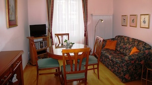 Una sala de estar acogedora con una mesa redonda de comedor, dos sillas, un sofá, un televisor y un radiador.