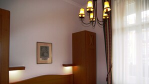 Un dormitorio con dos camas, un armario de madera, un cuadro enmarcado en la pared y una araña.