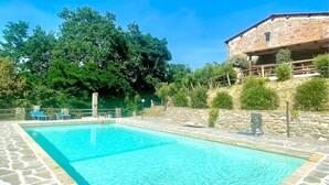 Une piscine rectangulaire revêtue de carrelage en pierre, entourée d’un mur de pierre et d’arbres.
