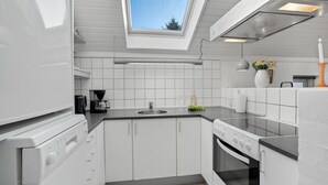Une cuisine compacte avec des meubles blancs, un four encastré, une machine à café et une lucarne.