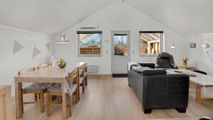 Un loft spacieux avec de hauts plafonds, un coin repas avec une table et des chaises en bois, un canapé en cuir noir et deux fenêtres donnant sur l’extérieur.