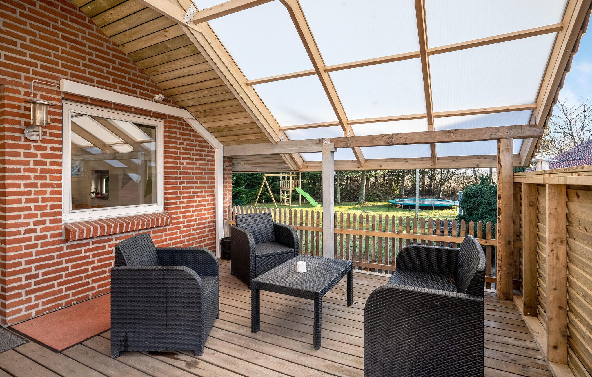 A covered patio with wicker furniture, a brick wall, and a view of a playground.