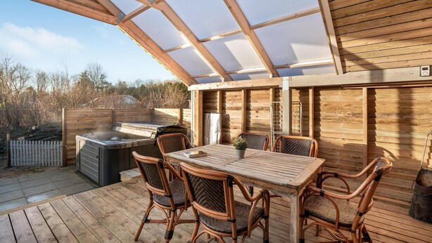 Un patio extérieur couvert avec une table en bois et des chaises en osier, un jacuzzi et un barbecue.
