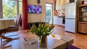 Eine moderne Küche mit weißen Schränken, einer eingebauten Mikrowelle und einem Kühlschrank. Es gibt eine Essecke mit Tisch und Stühlen sowie einen an der Wand befestigten Fernseher.