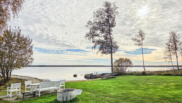 Un espace vert avec des bancs et un panneau indicateur, offrant une vue sur un lac paisible bordé d’arbres et surplombé d’un ciel nuageux.