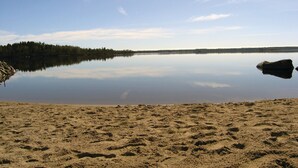Un lac paisible, avec une plage de sable et une rive bordée d’une forêt.