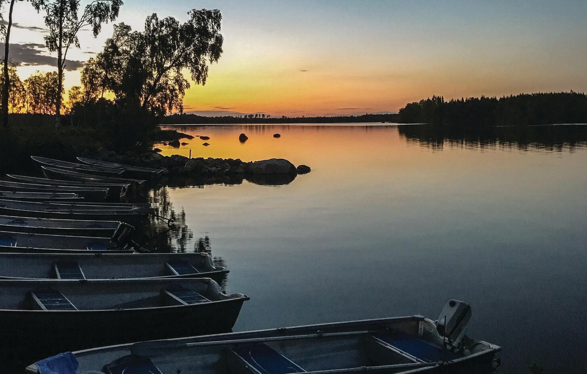 Un lac paisible au coucher du soleil, avec des bateaux amarrés sur la rive gauche.