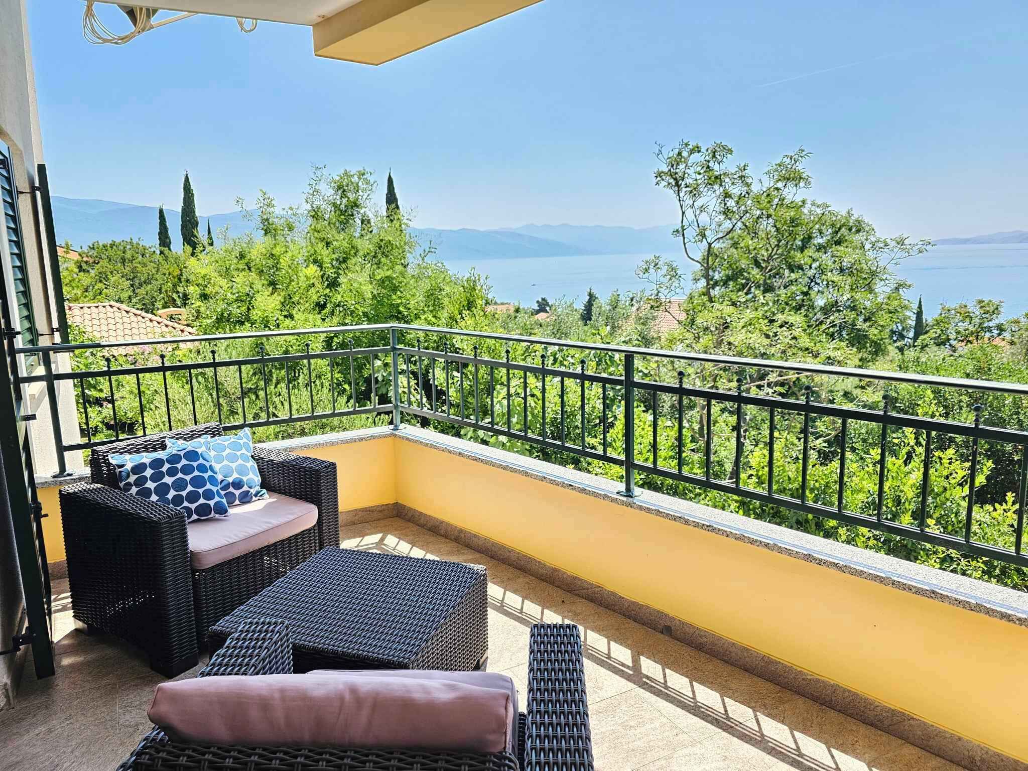 A balcony with wicker furniture, a yellow wall, and a view of greenery and mountains.